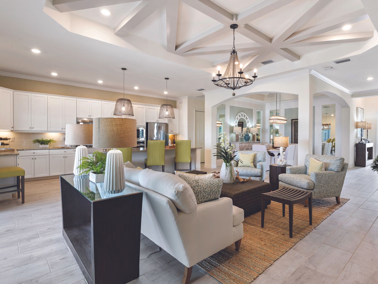 Open living and kitchen area under a white tray ceiling with crossed beams radiating from a central chandelier